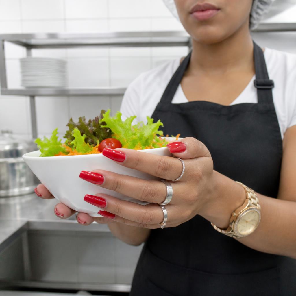 Mãos com unhas postiças, esmalte, anéis e relógio segurando um bowl de salada